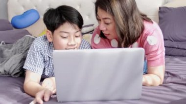 Mutlu aile anne ve oğlu dizüstü bilgisayar ile izlerken yüzünü gülümseme, hareket 4 k Asya Aile dinlenme yatakta dizüstü bilgisayar ile yavaş
