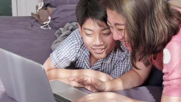 幸せな家族母親と息子でラップトップ コンピューターを見て顔を笑顔 遅いモーション アジア家族残りでラップトップ コンピューターのベッドの上 — ストック動画