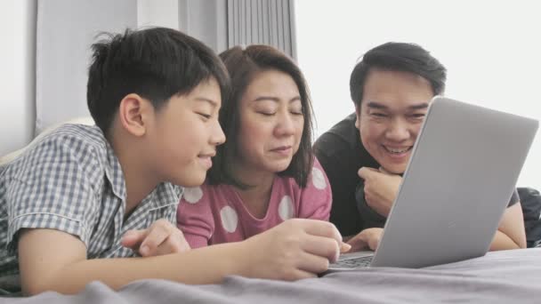 幸せな家族の父母と息子のラップトップ コンピューターを見て 楽しんで ラップトップ コンピューターが付いているベッドにスローモーション アジア家族の残り — ストック動画