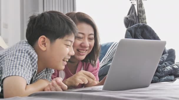 幸せな家族母親と息子でラップトップ コンピューターを見て顔を笑顔 遅いモーション アジア家族残りでラップトップ コンピューターのベッドの上 — ストック動画