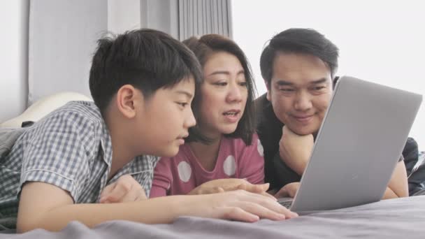 幸せな家族の父母と息子のラップトップ コンピューターを見て 楽しんで ラップトップ コンピューターが付いているベッドにスローモーション アジア家族の残り — ストック動画