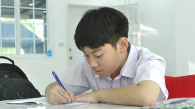 Asyalı çocuk beyaz masada ödev ağır çekim. Oturma odasında ödev ciddi Asyalı çocuk. Nasıl dahi yapılır.