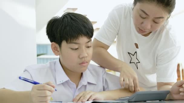 白いテーブルで宿題をしている彼女の息子を助けてアジアの母のスローモーション リビングで宿題の息子と深刻なアジアの母 お母さんが息子を教えている天才の作り方 — ストック動画