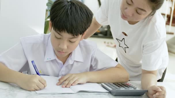 白いテーブルで宿題をしている彼女の息子を助けてアジアの母のスローモーション リビングで宿題の息子と深刻なアジアの母 お母さんが息子を教えている天才の作り方 — ストック動画