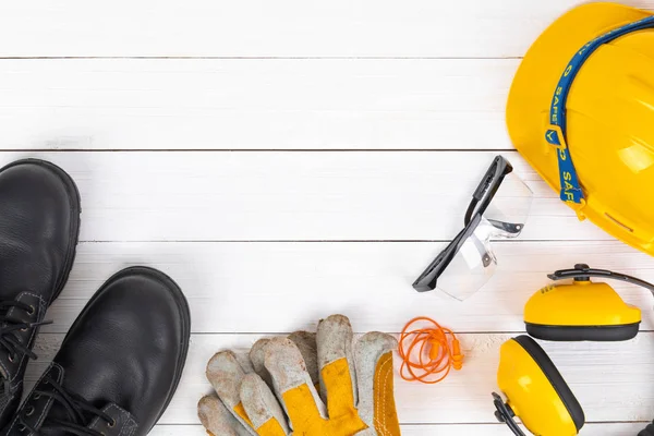 Banner image of construction safety gear including a hard hat,  safety shose ,goggles, and leather gloves flat lay on white wooden surface with copy space - Image