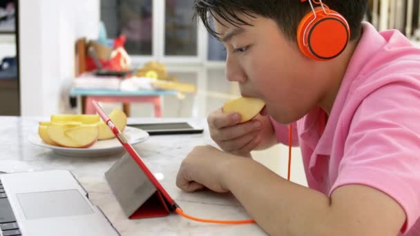 タブレットコンピュータで遊ぶ幸せなアジアの少年 リンゴを食べてタブレットで見ている少年 — ストック動画