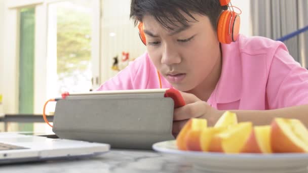 Gelukkig Aziatisch Spelen Tablet Met Oranje Hoofdtelefoon Teenage Jongen Eten — Stockvideo