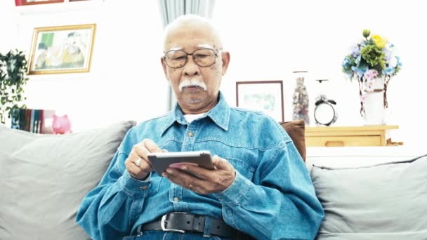 スマート フォンやタブレットを自宅で技術との祖父の幸せを手に使用して白い口髭のアジア シニア男 スローモーション ドリー ショット — ストック動画