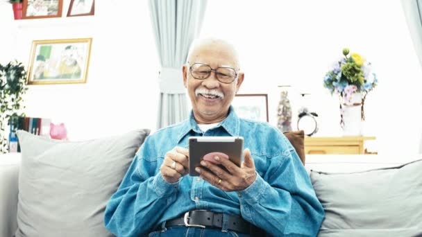 スマート フォンやタブレットを自宅で技術との祖父の幸せを手に使用して白い口髭のアジア シニア男 スローモーション ドリー ショット — ストック動画