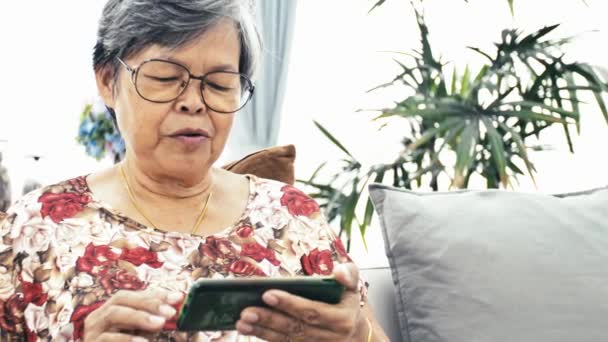 アジア高齢女性のスマート フォン 自宅の技術で幸せな祖母を手に使用します スローモーション ドリー ショット — ストック動画