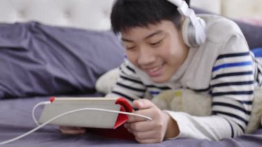 Tablet bilgisayarda izlemek ve gülümsemek yüz beyaz kulaklık giyen Asya yakışıklı UHD Dolly ateş.
