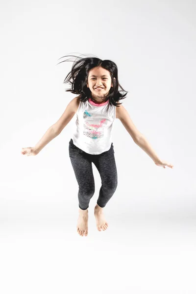 Asiatische lustige Kind Mädchen springen auf grauem Hintergrund. Stockbild