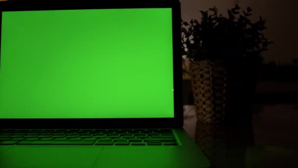リビングルームの机の上に緑色のクロマキースクリーンを表示するラップトップコンピュータ 暖かいライトが点灯した夕方の居心地の良いリビングルームの背景に ドリーは右から左へ撃った4K — ストック動画