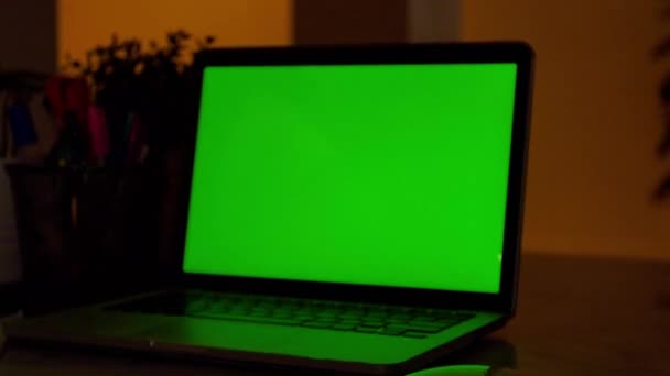 リビングルームの机の上に緑色のクロマキースクリーンを表示するラップトップコンピュータ 暖かいライトが点灯した夕方の居心地の良いリビングルームの背景に ズームインショット — ストック動画