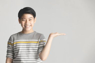 Asya preteen gri arka plan üzerinde yandan bir şey sunan.