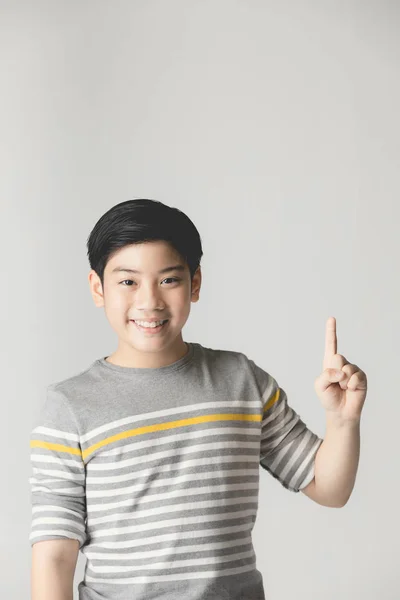 Asiatiska preteen Teenage Boy pekar upp över grå bakgrund. — Stockfoto