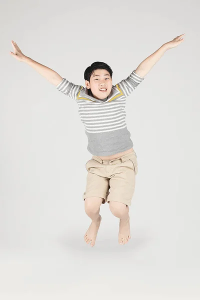 Asian śmieszne dziecko chłopiec skoki na szarym tle. — Zdjęcie stockowe