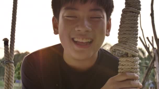肖像的亚洲男孩玩秋千与日落耀斑在家里 手持慢动作青少年摆动与微笑的脸 — 图库视频影像