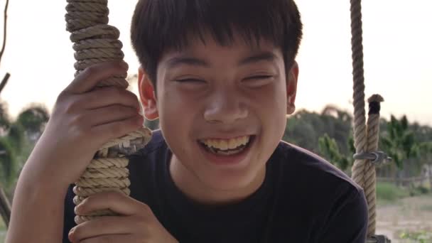 肖像的亚洲男孩玩秋千与日落耀斑在家里 手持慢动作青少年摆动与微笑的脸 — 图库视频影像