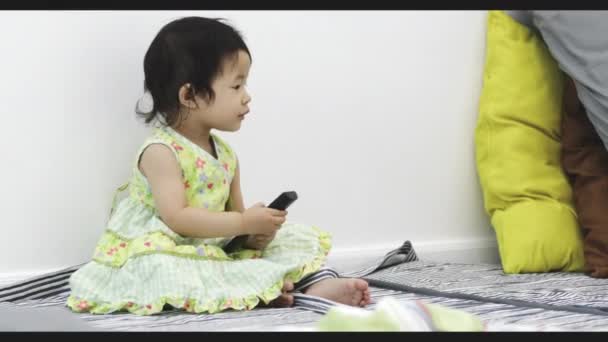 リビングルームでリモコンを持つ幸せなアジアの女の子 4Kハンドヘルド幸せな子供リラックス — ストック動画