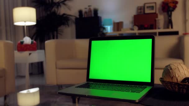 显示绿色色度键屏幕的笔记本电脑矗立在客厅的办公桌上 在背景舒适的客厅在晚上与温暖的灯打开 — 图库视频影像