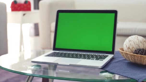 リビングルームの机の上に緑色のクロマキースクリーンを表示するラップトップコンピュータ 背景に居心地の良いリビングルーム ショットでドリーズーム — ストック動画