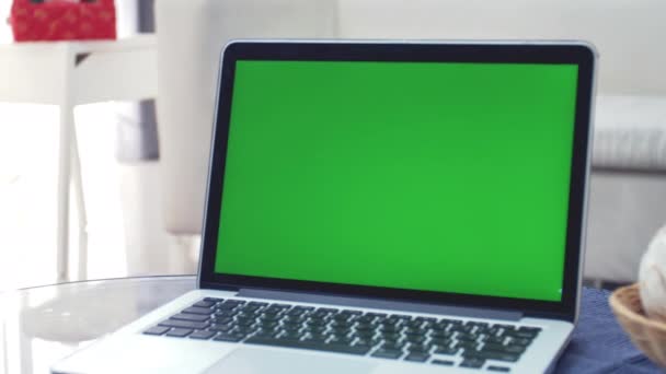リビングルームの机の上に緑色のクロマキースクリーンを表示するラップトップコンピュータ 背景に居心地の良いリビングルーム ドリーズームアウトショット — ストック動画