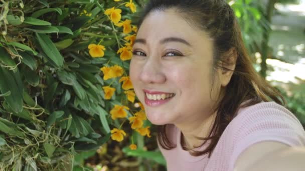 快乐的亚洲女人在花园里用美丽的兰花拍照 — 图库视频影像