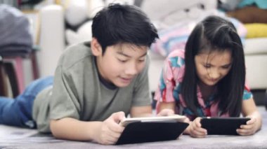 Evde tablet veya akıllı telefon ile oynayan çocuk , Asyalı erkek ve kız gülümseyen yüzleri ile birlikte cep telefonu oyunu oynuyor.
