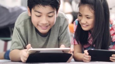 Evde tablet veya akıllı telefon ile oynayan çocuk , Asyalı erkek ve kız gülümseyen yüzleri ile birlikte cep telefonu oyunu oynuyor.