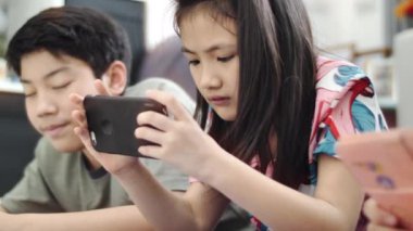 Evde tablet veya akıllı telefon ile oynayan çocuk , Asyalı erkek ve kız gülümseyen yüzleri ile birlikte cep telefonu oyunu oynuyor.