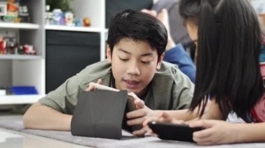 Evde tablet veya akıllı telefon ile oynayan çocuk , Asyalı erkek ve kız gülümseyen yüzleri ile birlikte cep telefonu oyunu oynuyor.