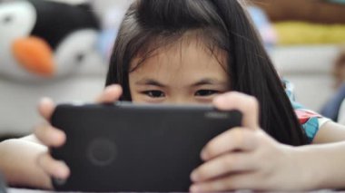 Evde tablet veya akıllı telefon oynayan çocuk kız , Akıllı kız gülümseme yüz ile cep telefonu oyunu oynuyor.