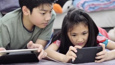 Evde tablet veya akıllı telefon oynayan çocuk , Asyalı erkek ve kız gülümseme yüz ile birlikte cep telefonu oyunu oynuyor.