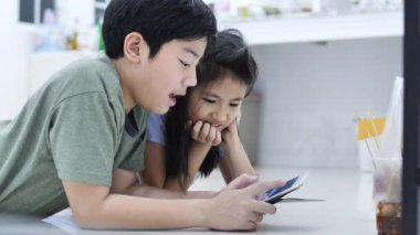 Evde tablet veya akıllı telefon oynayan çocuk , Asyalı erkek ve kız gülümseme yüz ile birlikte cep telefonu oyunu oynuyor.