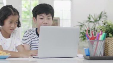 Genç Asyalı oğlan ve kız evde dizüstü bilgisayarla oynuyorlar. Çocuklar birlikte bir dizüstü bilgisayarda online oyun oynuyorlar. Dolly 60 fps attı..