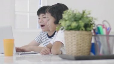 Genç Asyalı oğlan ve kız evde dizüstü bilgisayarla oynuyorlar. Çocuklar birlikte bir dizüstü bilgisayarda online oyun oynuyorlar. Dolly 60 fps attı..