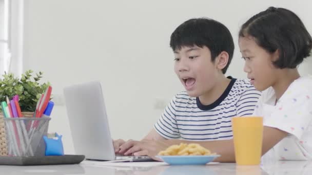 自宅でラップトップコンピュータで遊んでいる若いアジアの男の子と女の子 子供たちは一緒にラップトップコンピュータでオンラインゲームをプレイしています ドリーショット60Fps — ストック動画