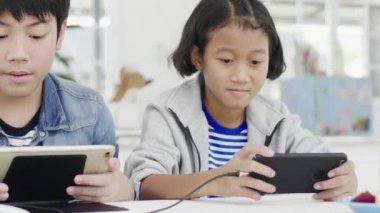 Yakın asya sevimli kız ve genç erkek akıllı telefonlar ve tablet rekabetçi video oyunu oynarken, yatay manzara modunda onları tutarak. Dolly Shot 60fps.