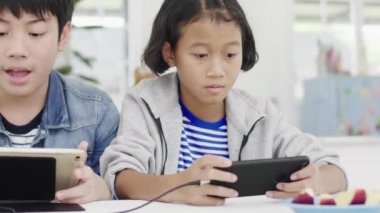 Yakın asya sevimli kız ve genç erkek akıllı telefonlar ve tablet rekabetçi video oyunu oynarken, yatay manzara modunda onları tutarak. Dolly Shot 60fps.