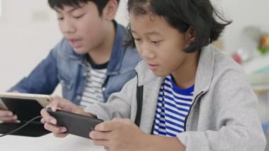 Yakın asya sevimli kız ve genç erkek akıllı telefonlar ve tablet rekabetçi video oyunu oynarken, yatay manzara modunda onları tutarak. Dolly Shot 60fps.