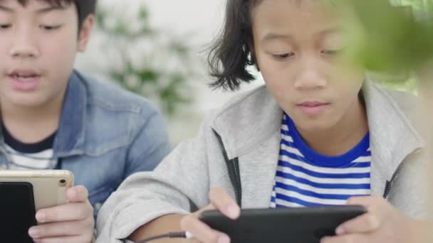 特写亚洲可爱的女孩和小男孩在智能手机和平板电脑上玩竞争视频游戏 在水平景观模式举行他们 60Fps在娃娃射击 — 图库视频影像