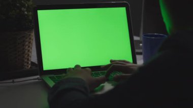 Masabaşında dizüstü bilgisayar kullanan genç bir çocuğun omzundan çekilmiş fotoğrafı, yeşil ekrana bakıyor. Dolly atış 60fps.