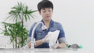 Asyalı genç çocuk evde mutfakta bulaşık yıkama, yaşam tarzı kavramı. Tayland modern evde lavaboda Genç yıkama çanak. 60fps