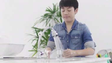 Asyalı genç çocuk evde mutfakta bulaşık yıkama, yaşam tarzı kavramı. Tayland modern evde lavaboda Genç yıkama çanak. 60fps