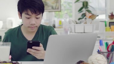 Akıllı telefon uygulamaları ile parşömen ler kullanarak Asyalı genç çocuk, yavaş yavaş evde ekmek bisküvi ve çikolata ile organik süt kahvaltı yiyor.