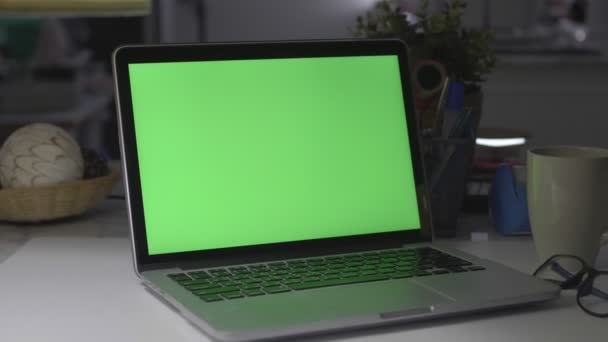 緑色の画面を備えたラップトップ 暗いオフィスだドリーが撃たれたあなた自身の画像やビデオを置くのに最適 — ストック動画