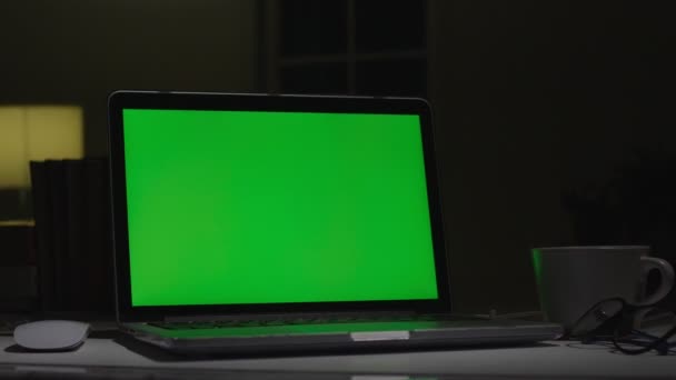 Ordinateur portable avec écran vert. Bureau sombre. Dolly a tiré. Parfait pour mettre votre propre image ou vidéo .