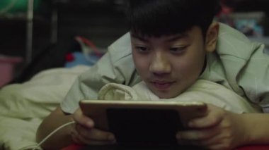 Genç Asyalı mutlu çocuk gülen yüzle tableti kullanıyor..