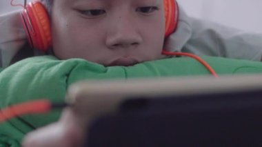 Genç Asyalı mutlu çocuk gülen yüzle tableti kullanıyor..